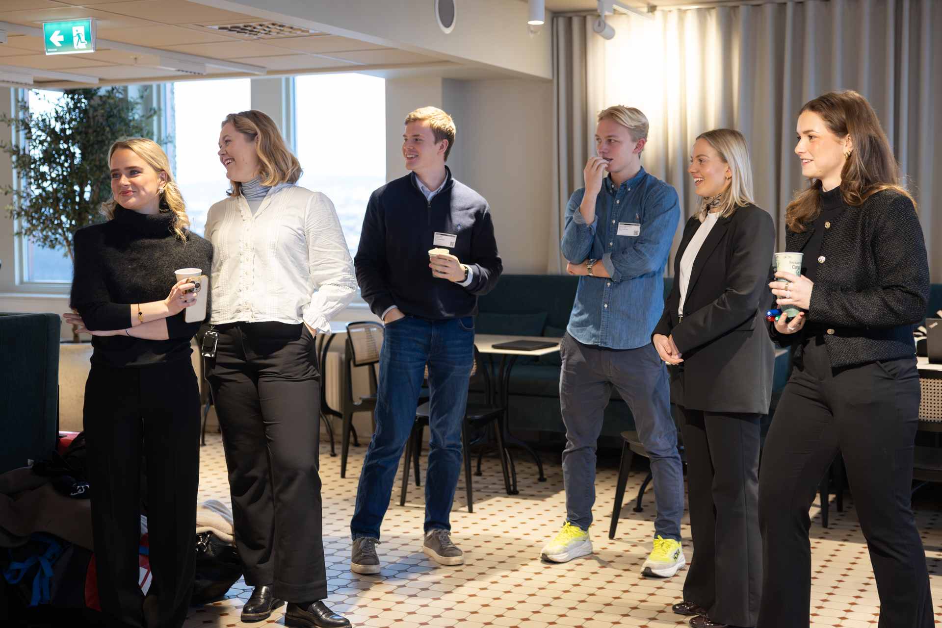 6 mennesker står og drikker kaffe.